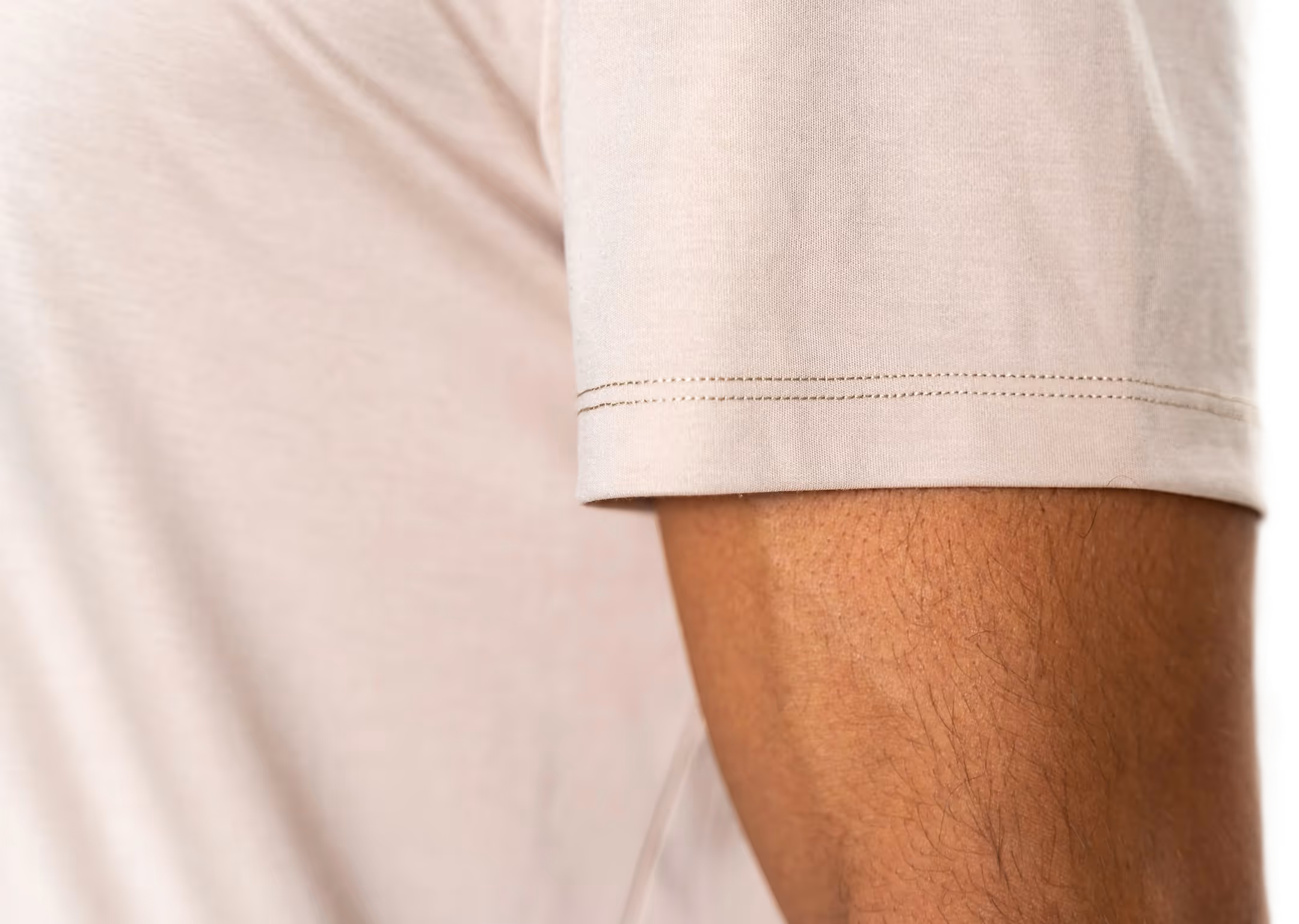 Close-up of a person's arm wearing a beige short-sleeve shirt with visible stitching on the sleeve.