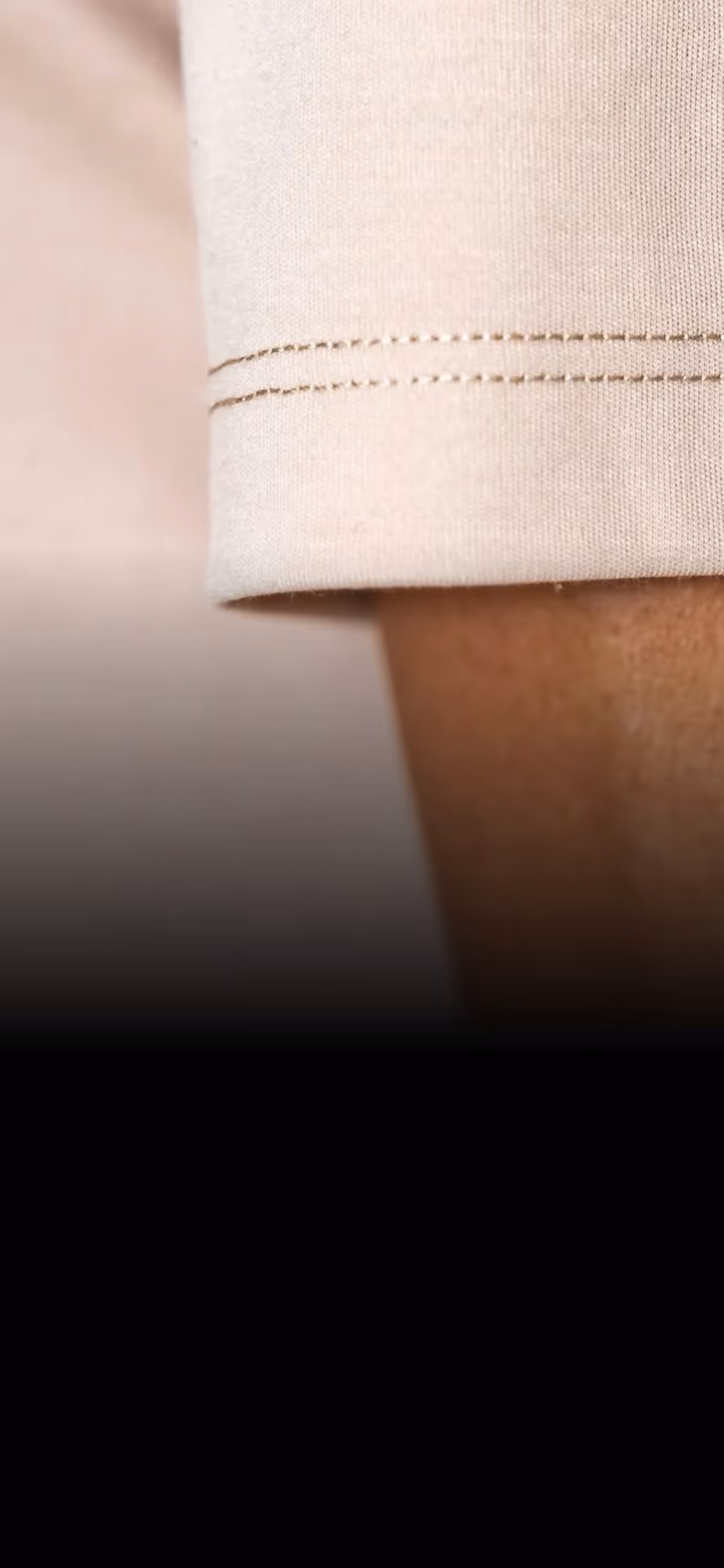 Close-up of beige fabric sleeve with double stitching above a person's wrist.