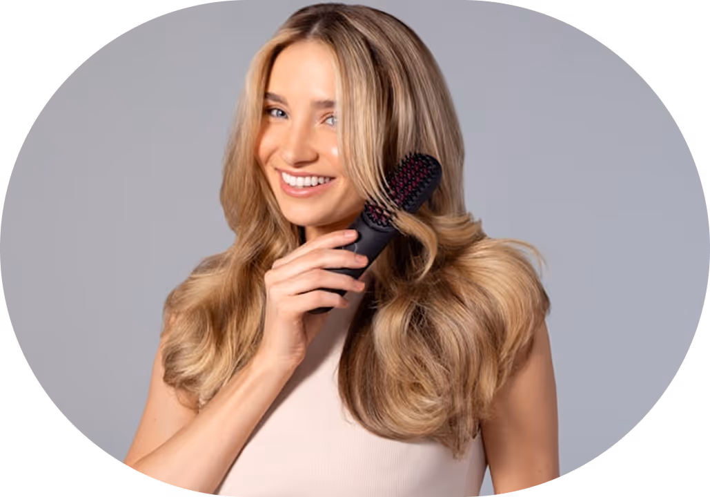 Smiling woman with long blonde hair using a black hairbrush against a gray background.