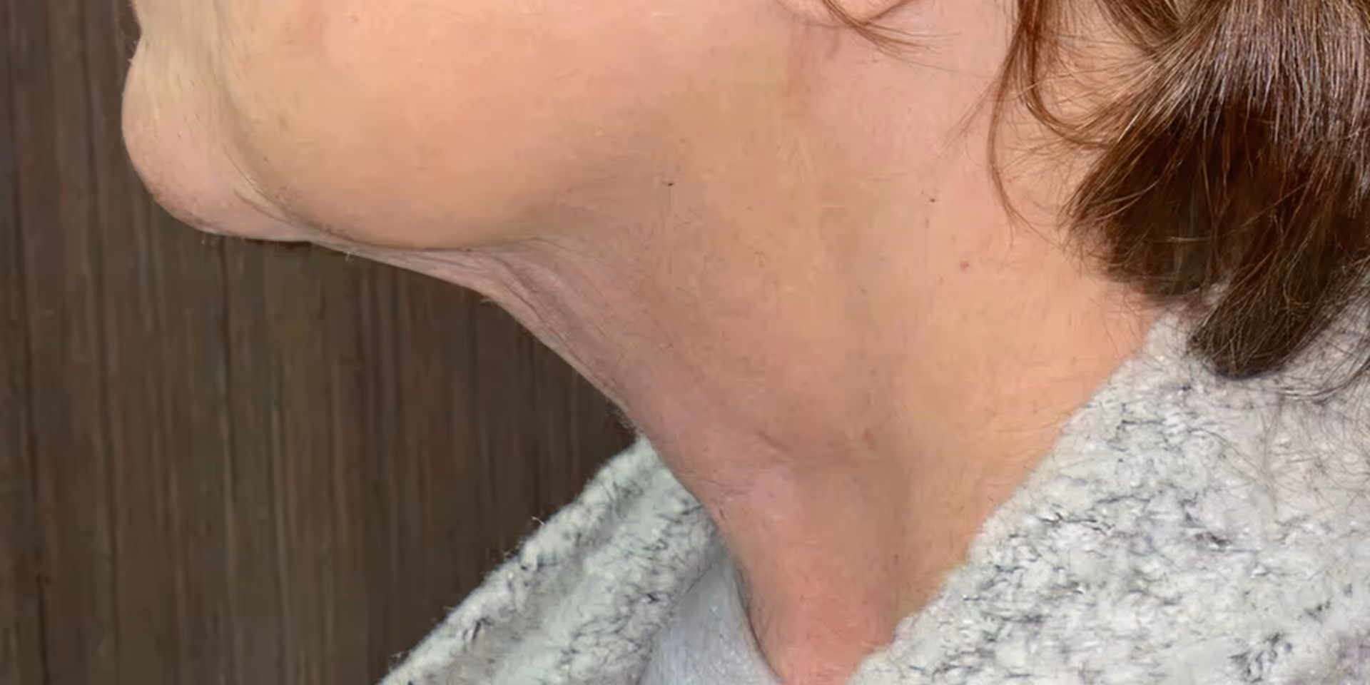 Side profile of an older woman with short brown hair and wearing a gray textured garment.