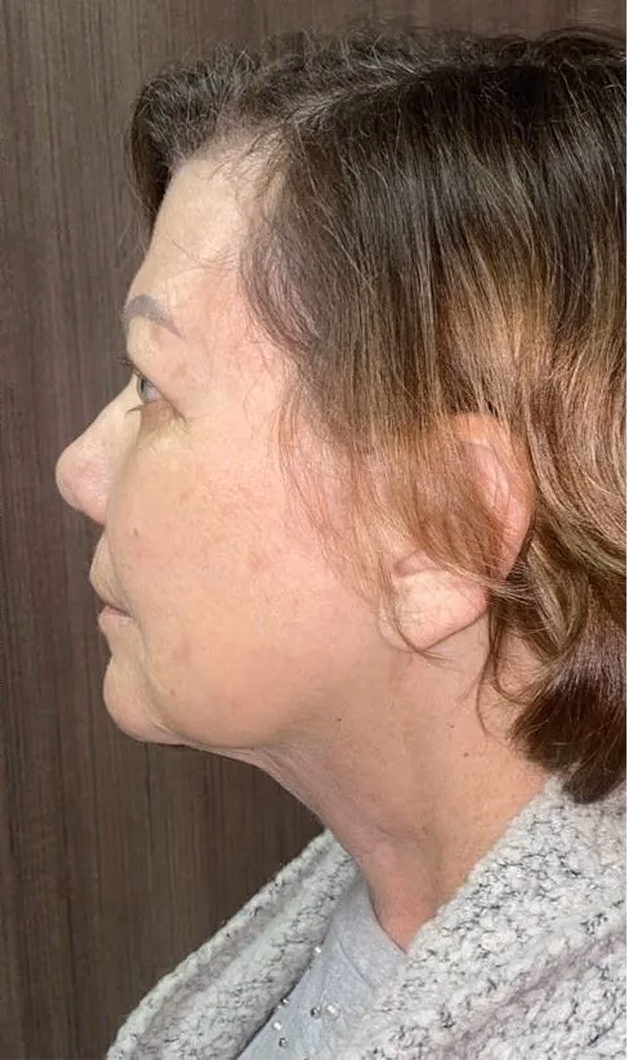 Side profile of an older woman with short brown hair and wearing a gray textured garment.