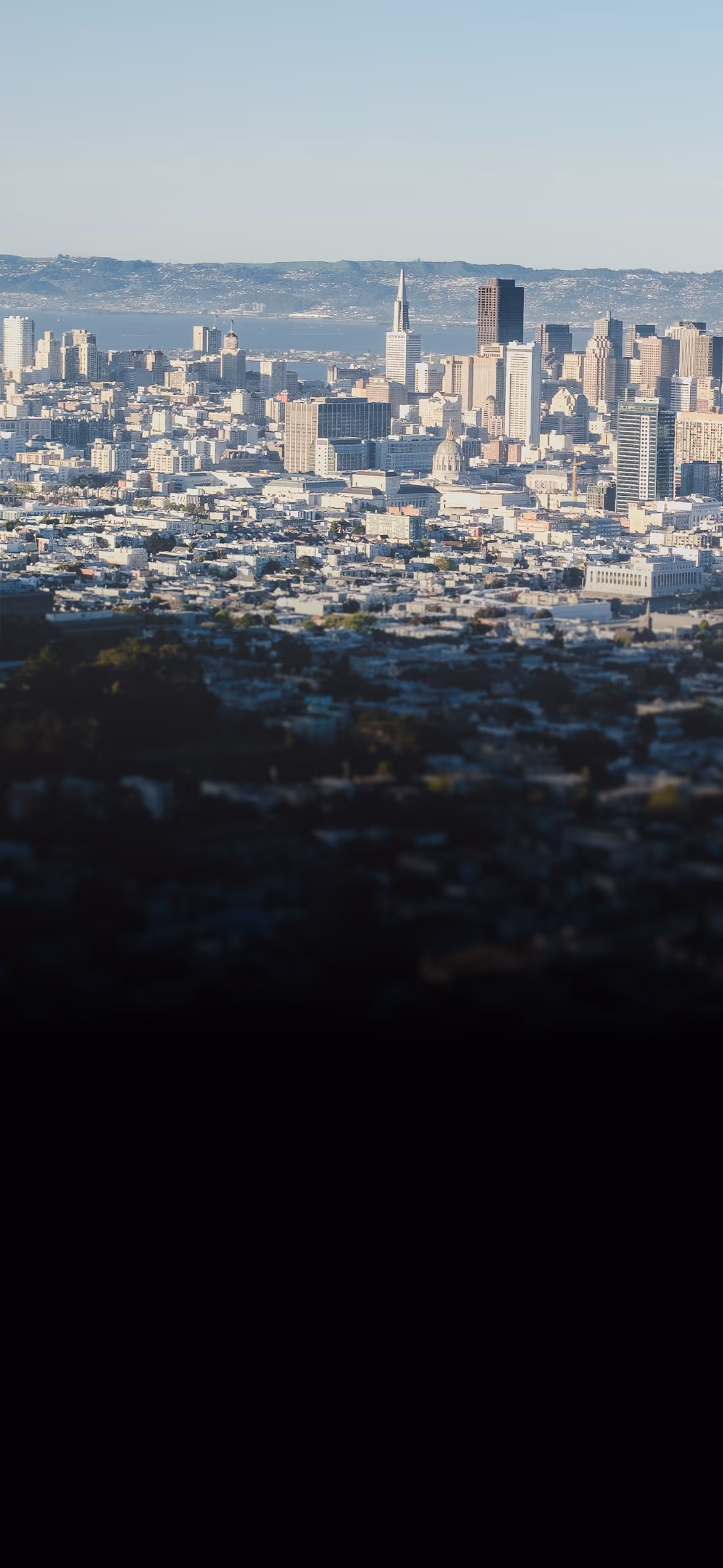 San Francisco cityscape with Bay Bridge, Transamerica Pyramid, and surrounding buildings under clear sky.