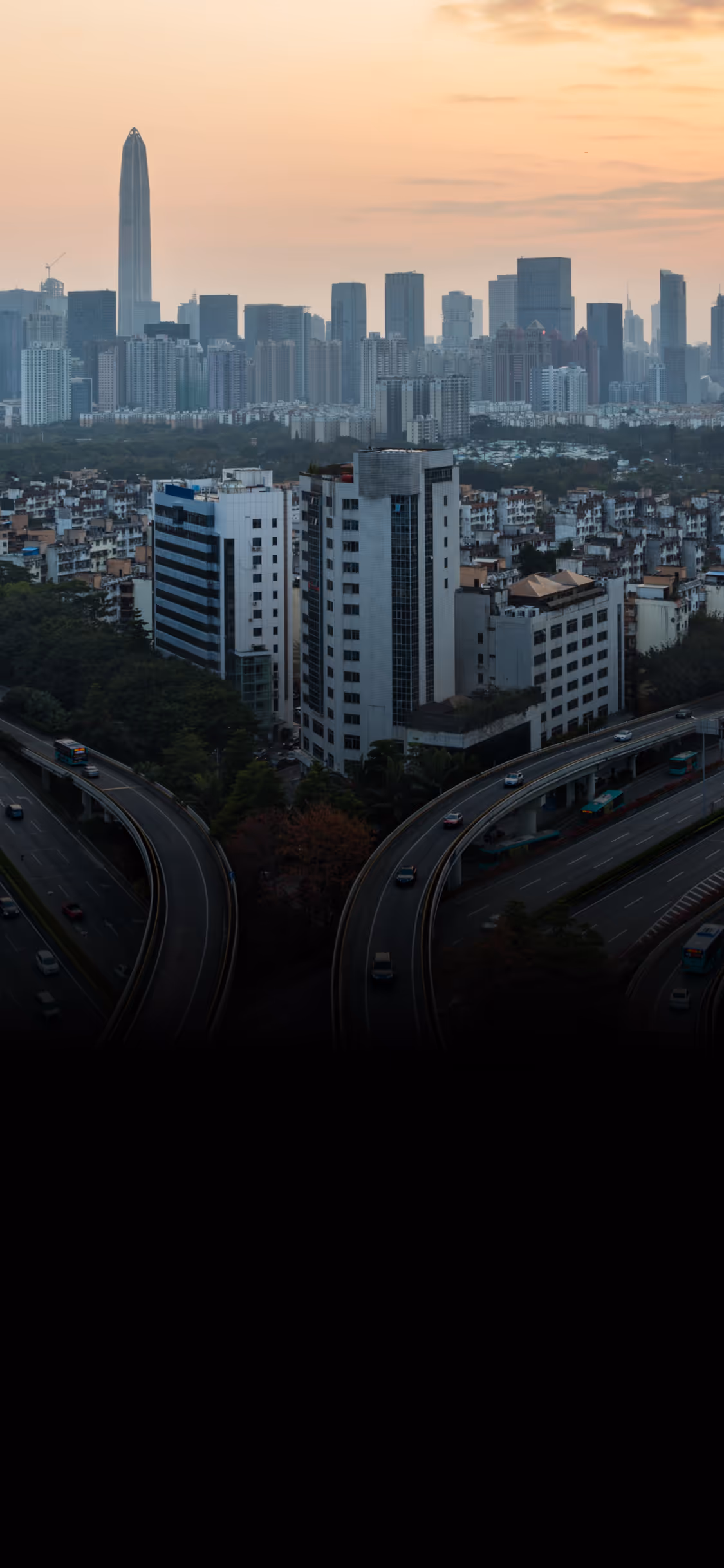 Curved highways and tall buildings in a cityscape at sunset with a prominent skyscraper.