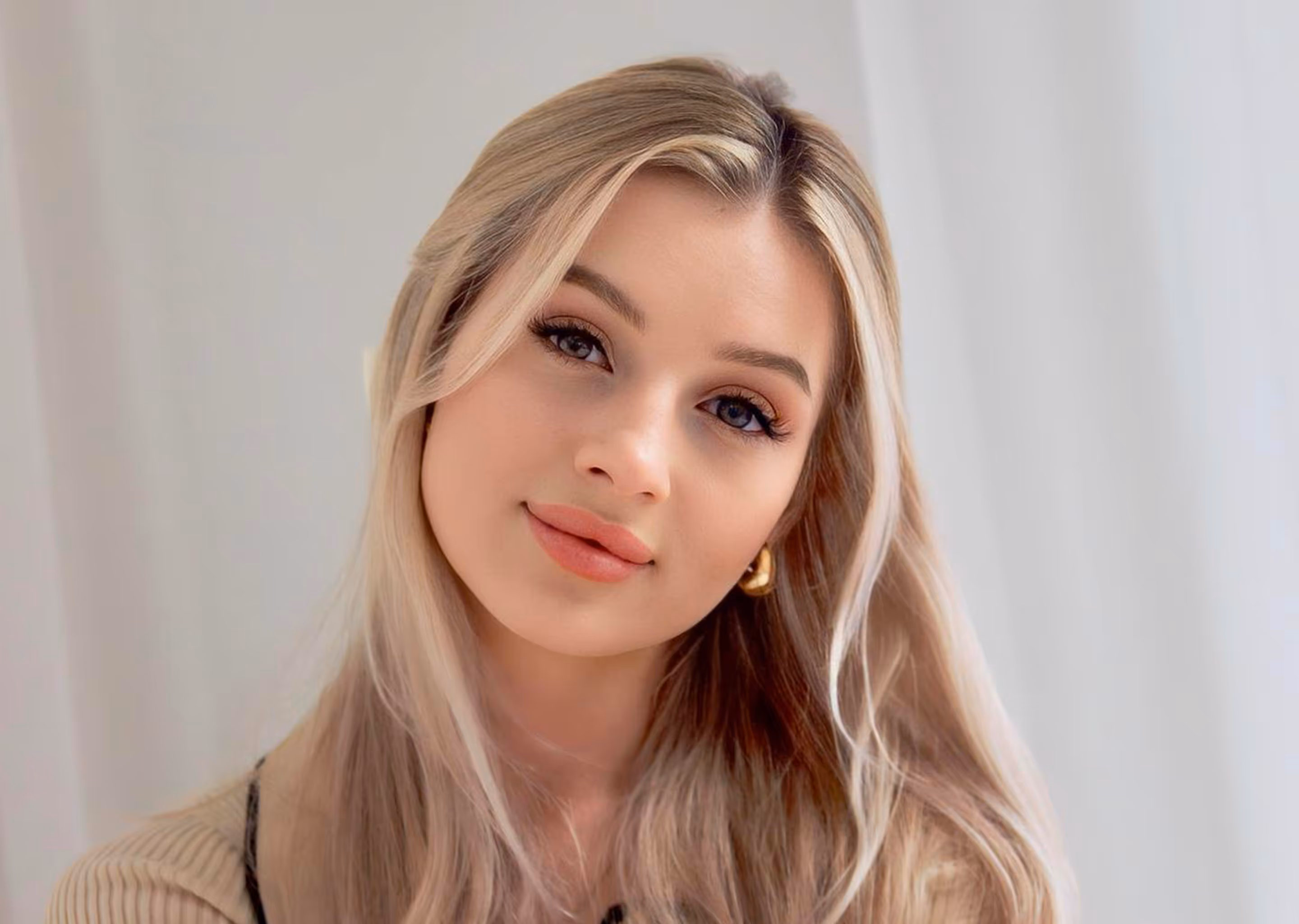 Close-up of a young woman with long blonde hair, natural makeup, and gold hoop earrings.