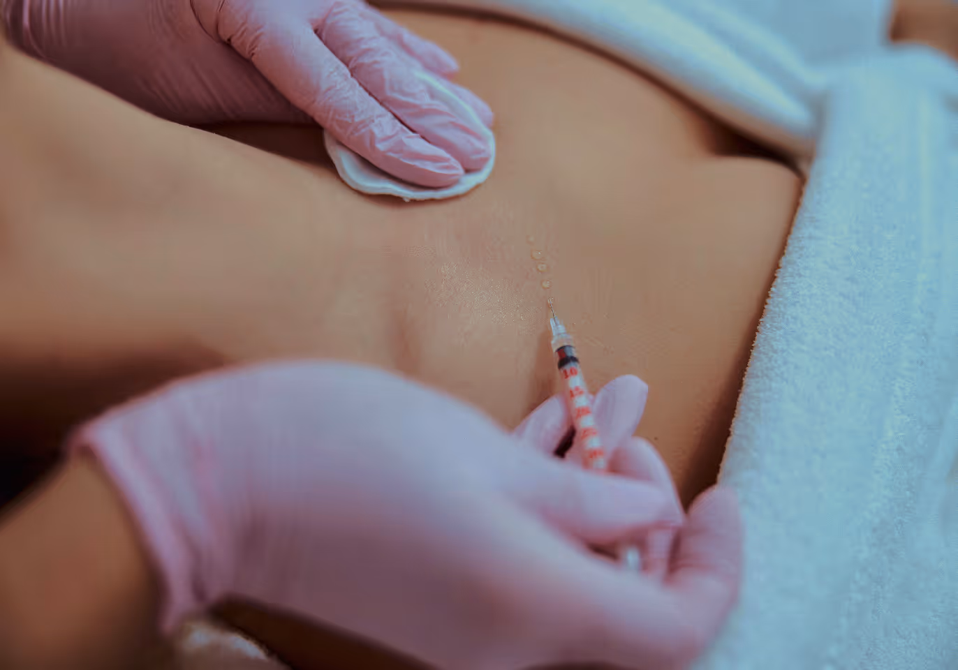 Gloved hands preparing skin with cotton pad before injecting with a syringe on a person's back.