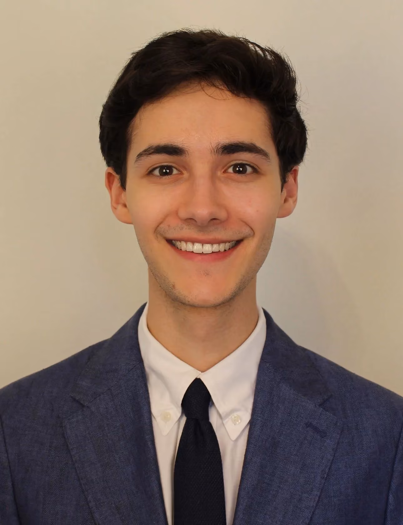 Smiling young man with dark hair in a blue suit jacket, white shirt, and black tie.