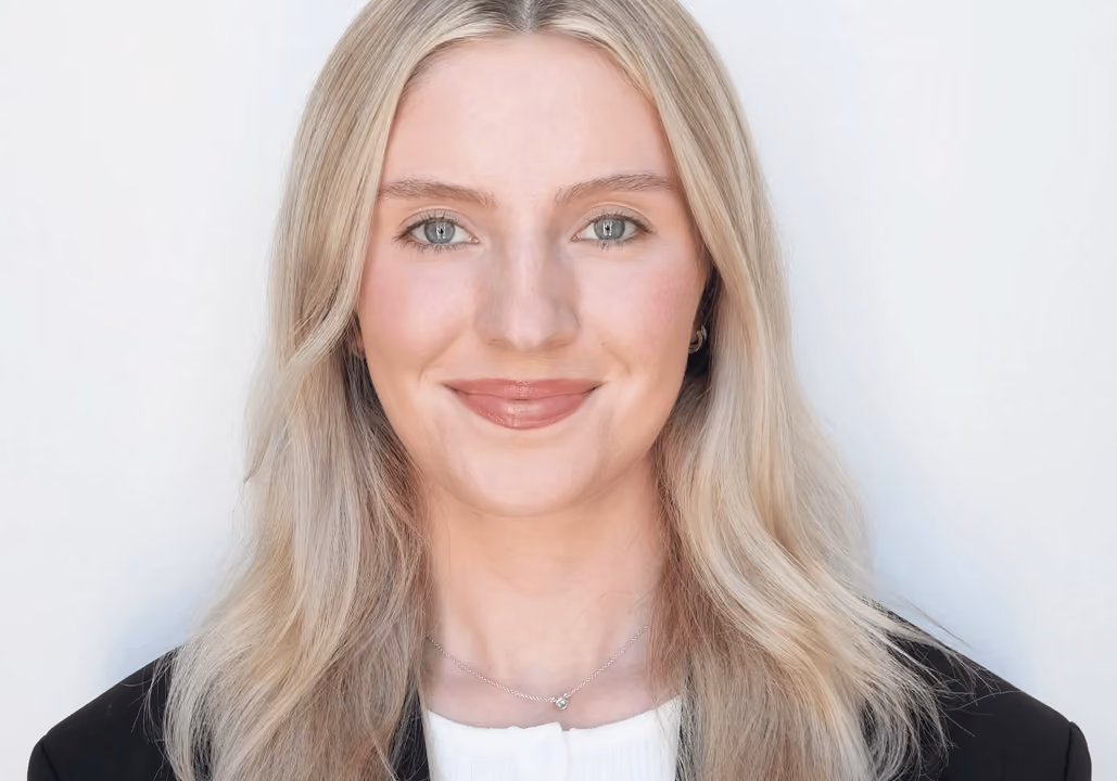 Smiling woman with long blonde hair wearing a black blazer and white top, against a white background.