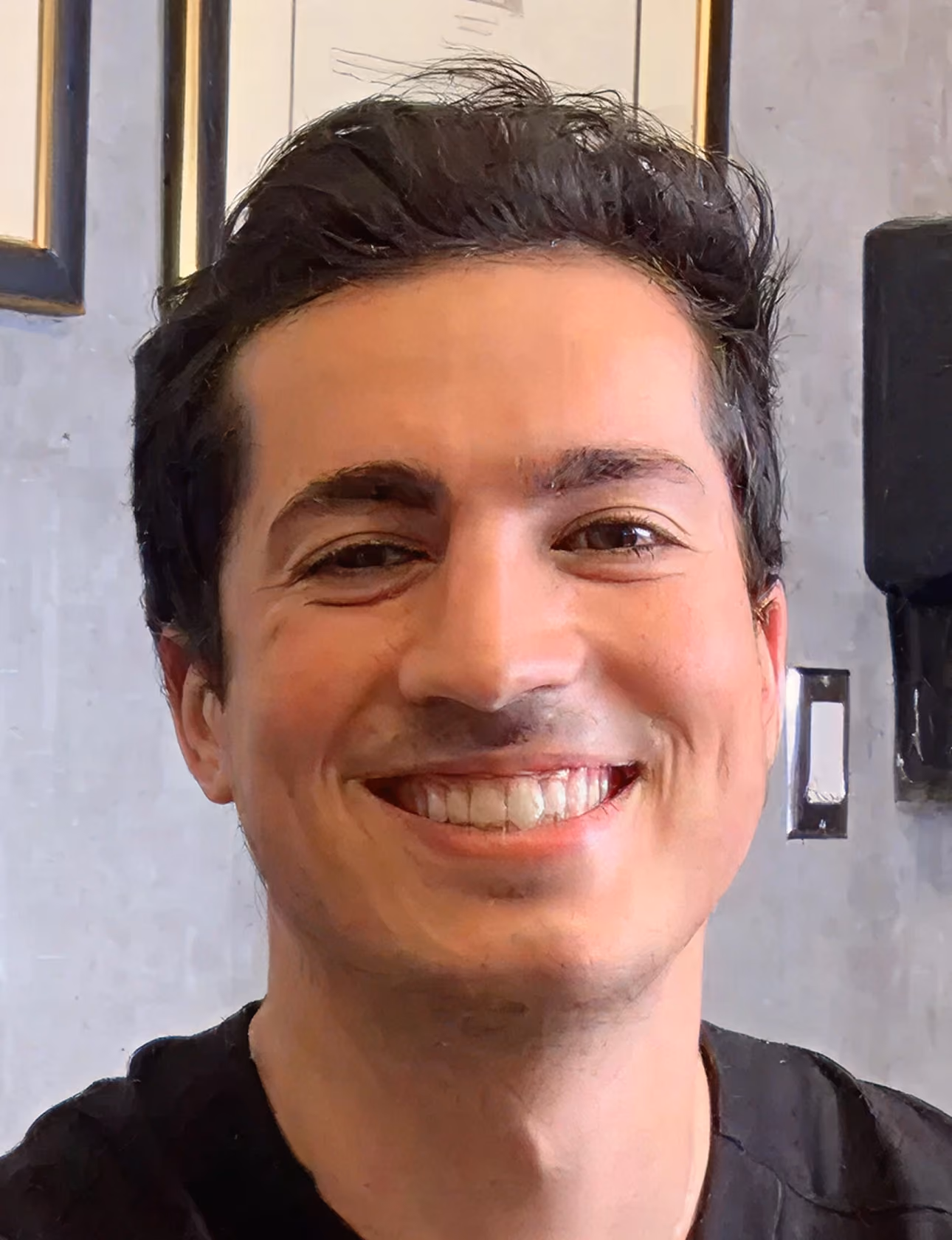 Smiling man with dark hair in a black shirt in an indoor setting.