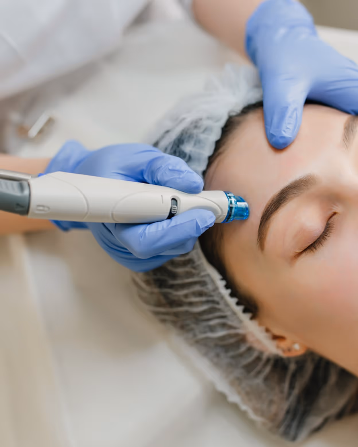 Close-up of a facial treatment with a handheld device on a woman's forehead by a gloved professional.