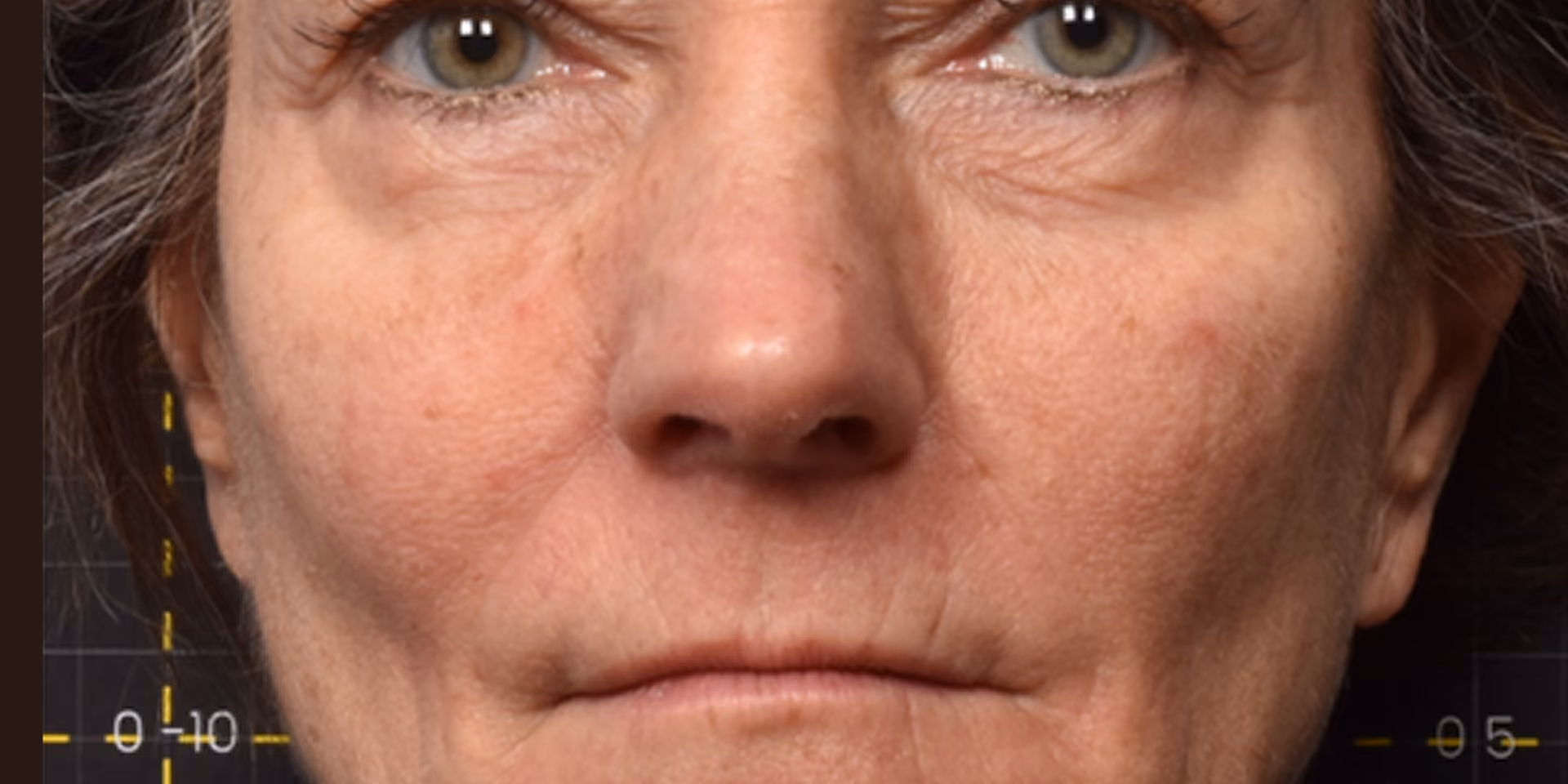 Close-up of a middle-aged woman's face showing natural skin texture, wrinkles, and light green eyes.