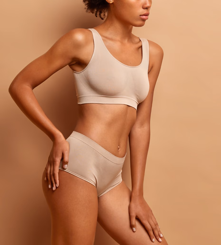 Woman wearing beige seamless underwear set posing against a beige background, showing midsection and upper thighs.