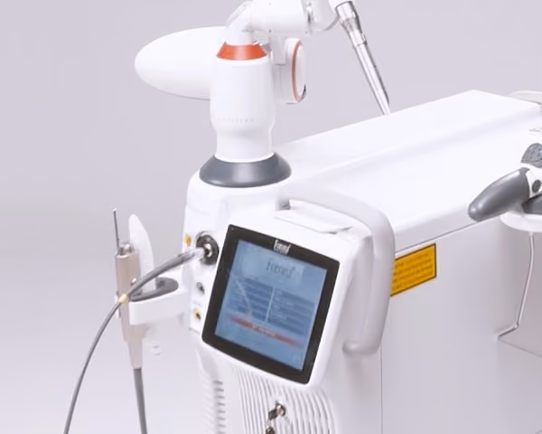 Close-up of a white medical laser device with a touchscreen displaying settings and various attached instruments on a neutral background.