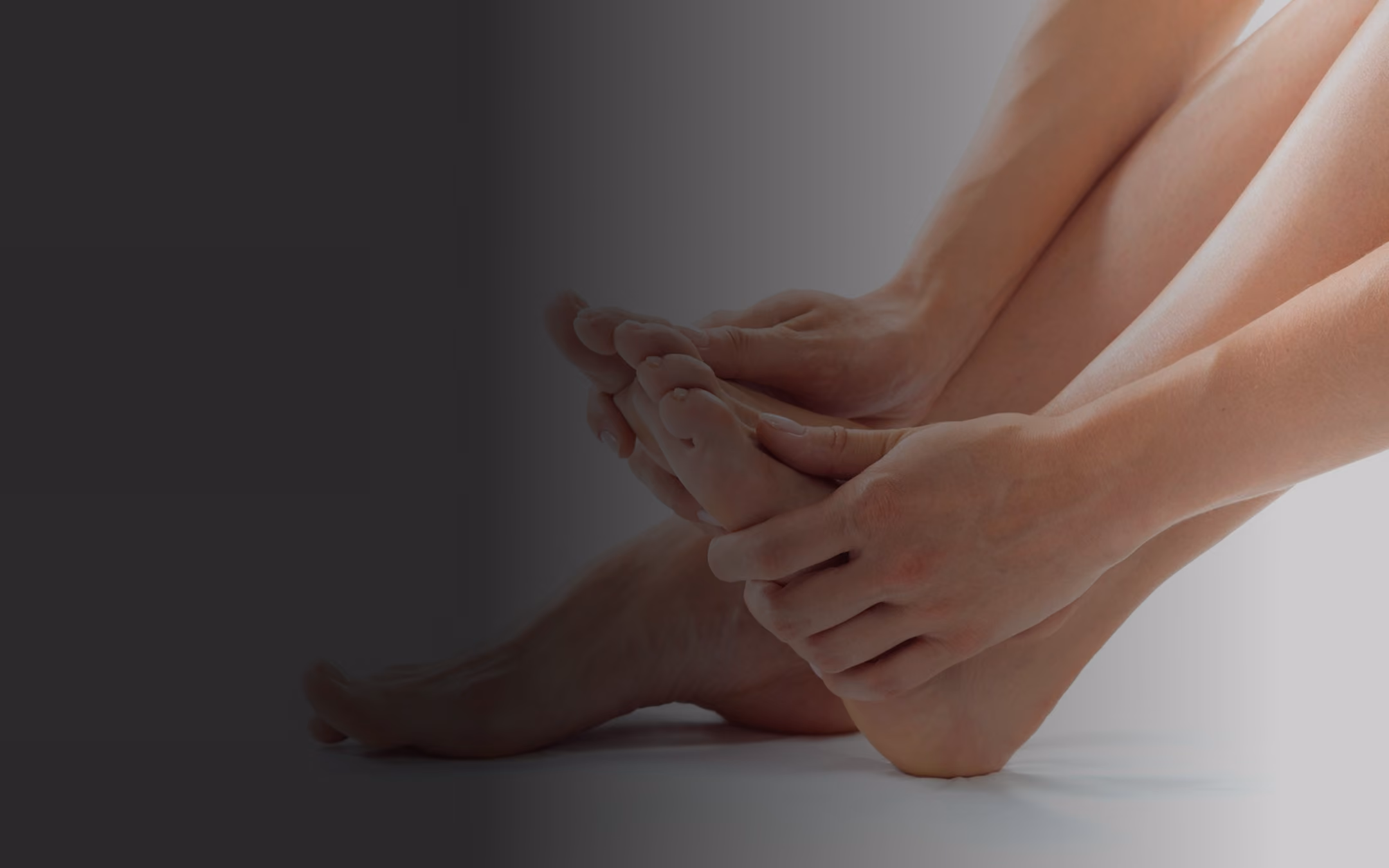 Hands gently holding and massaging a bare foot against a neutral background.