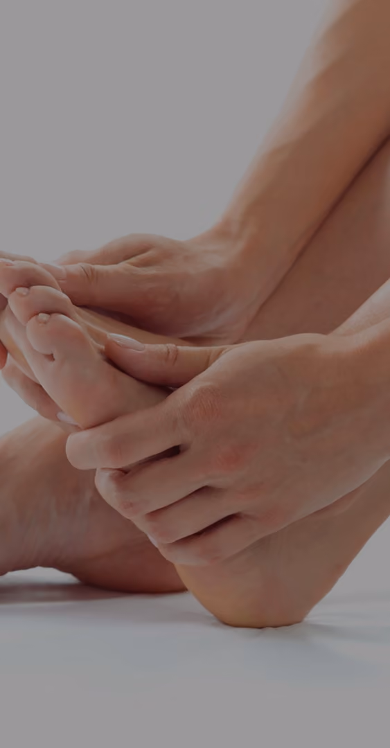 Hands gently holding and massaging a bare foot against a plain light background.