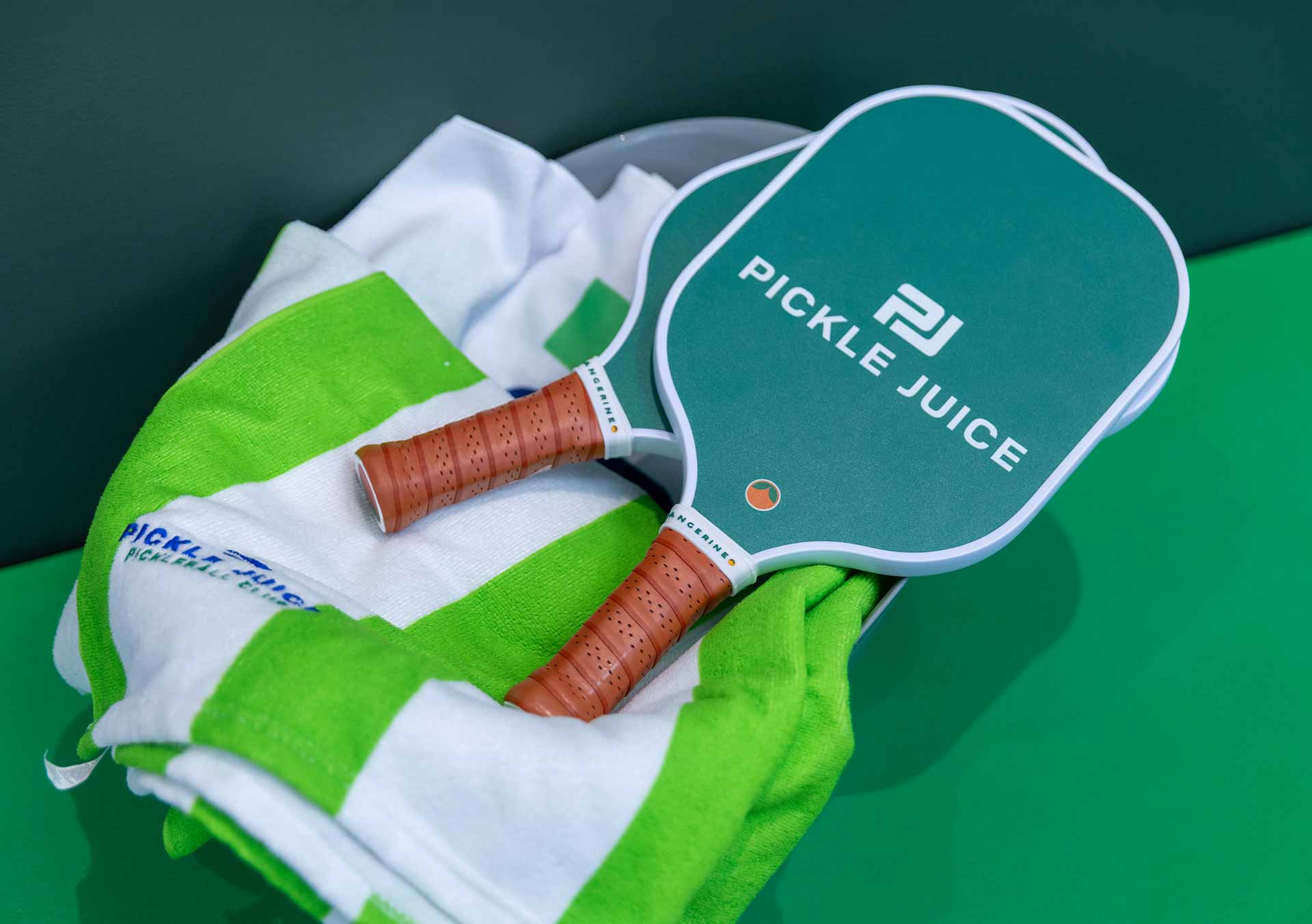 Two Pickle Juice pickleball paddles with brown handles resting on a green and white towel.