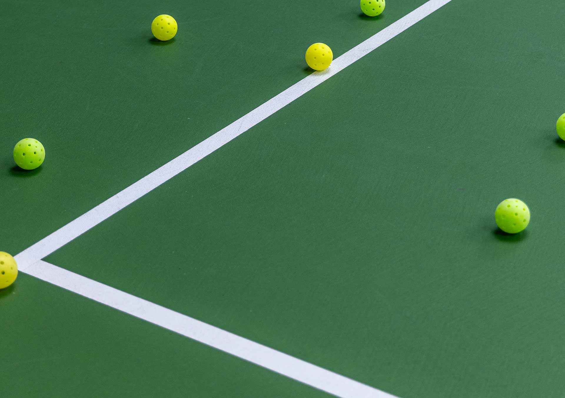 Yellow pickleball balls scattered on a green pickleball court near white boundary lines.
