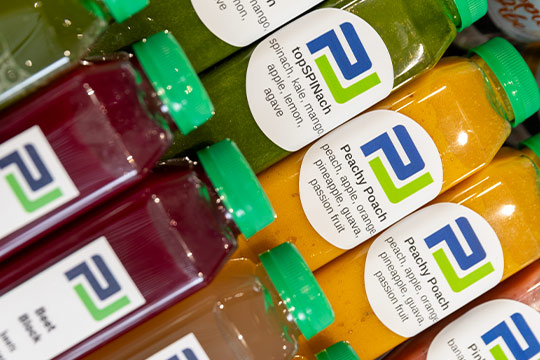 Rows of colorful bottled juices labeled with flavors like top spinach and peachy poach.