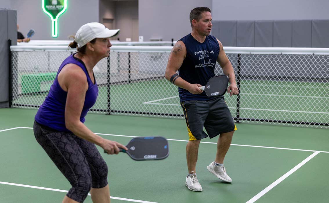 Man and woman playing pickleball indoors, holding paddles and focused on the game.