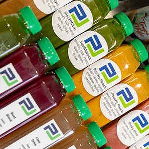 Rows of colorful bottled juices with green caps and labels showing flavor names and the Pickle Juice logo.