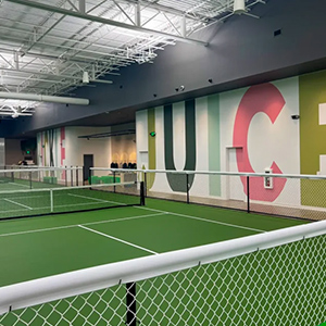 Indoor pickleball court with green floor and large colorful letters on the wall.
