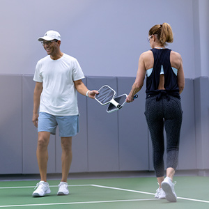 Man and woman playing pickleball on an indoor court tapping paddles and smiling.