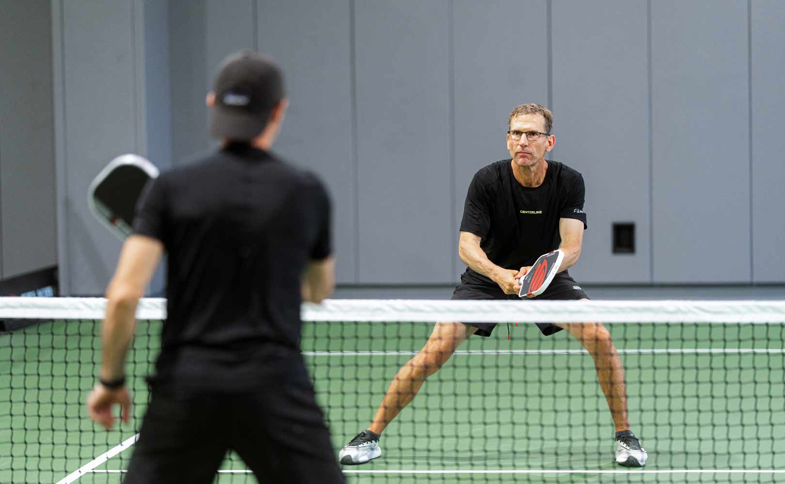 Two men playing pickleball on an indoor court with paddles preparing for a shot.