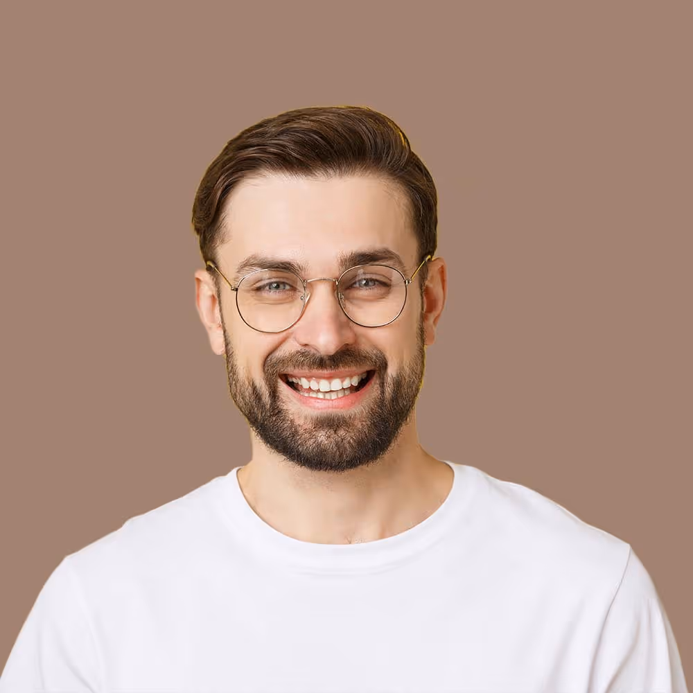 Smiling bearded man with glasses wearing a white shirt against a brown background.