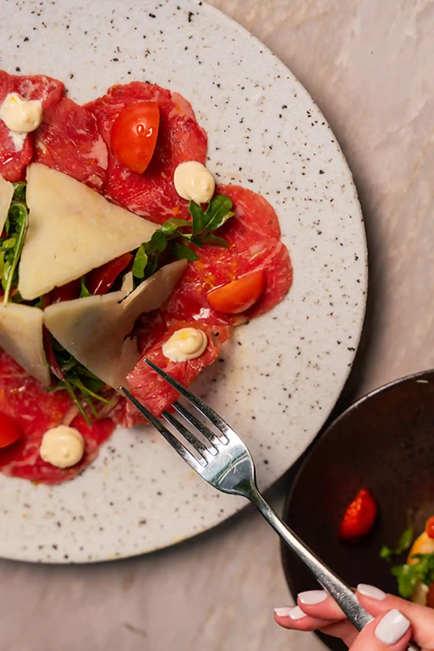 Thinly sliced beef carpaccio topped with arugula, shaved parmesan, and cherry tomatoes, served at Ziva Miami.