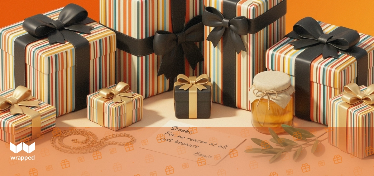 Sunlit table with a gold necklace, ribboned gift box, jar of honey and a handwritten message card among olive leaves