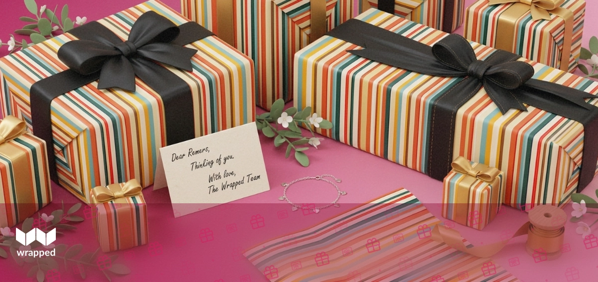 Handwritten message card beside a silver bracelet, folded gift wrap and a ribbon spool on a soft rose editorial backdrop