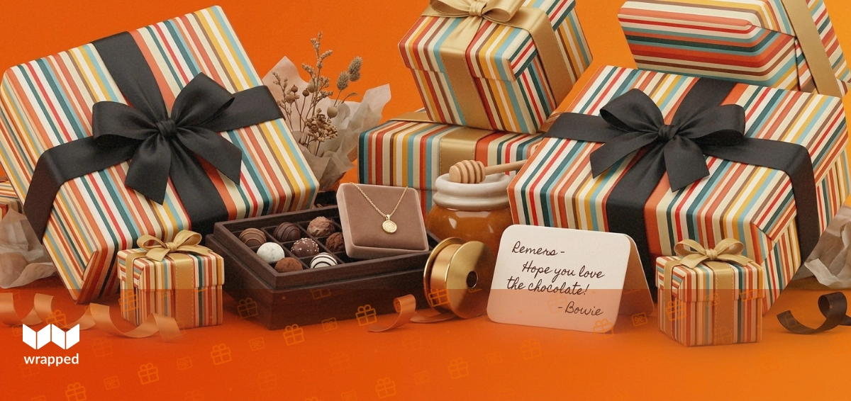 Editorial still life of a chocolate truffle box, gold necklace, ribbon spool and honey jar on a warm amber table