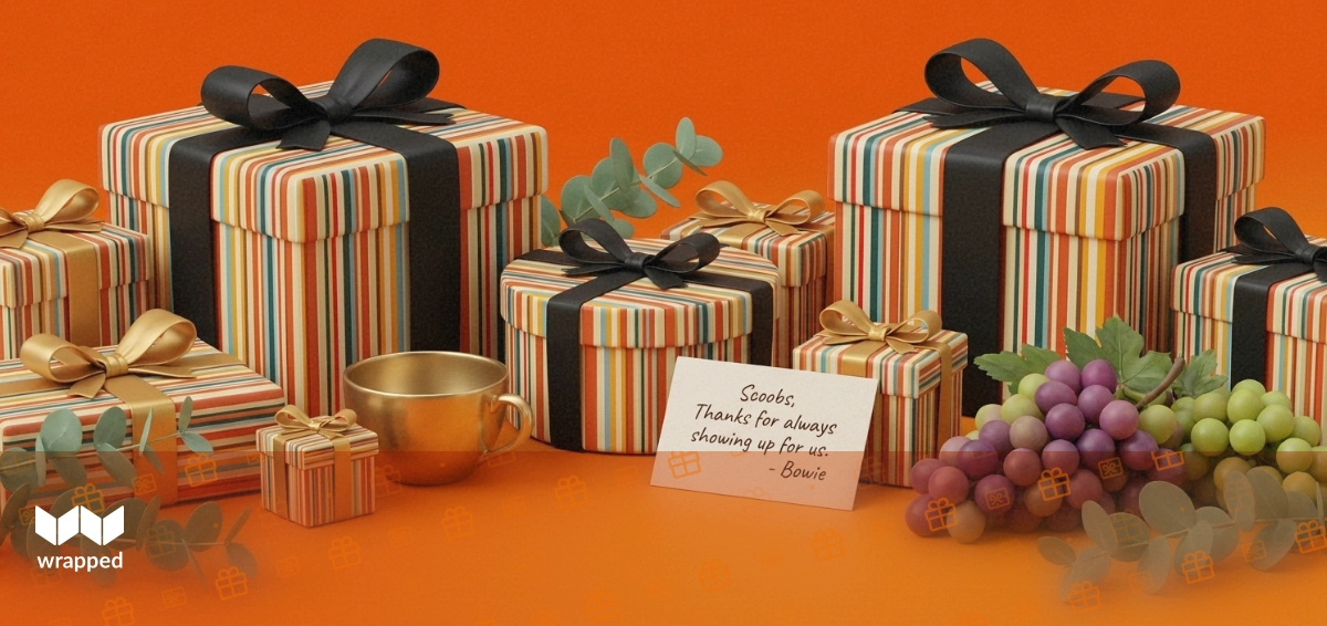 Warm amber table scene with a round gift box, brass tea cup, handwritten message card, grapes and eucalyptus sprig