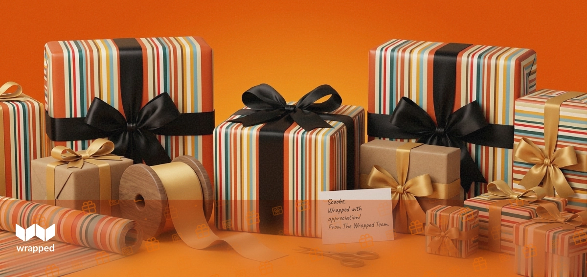 Kraft gift box with satin ribbon, wrapping paper roll, handwritten message card and brass scissors on a warm amber surface