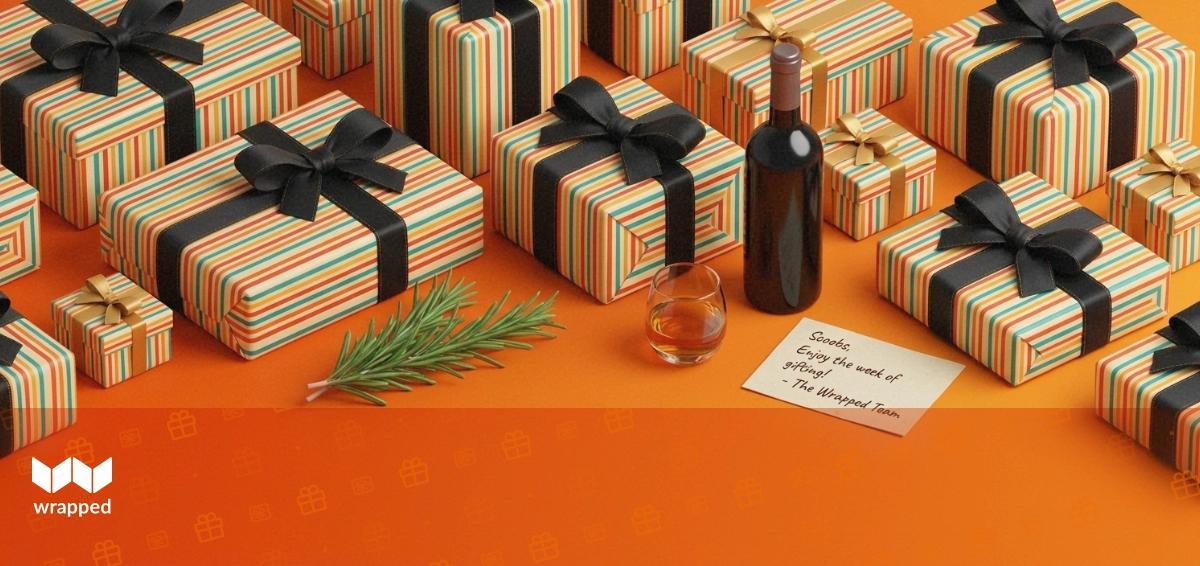 Editorial still life of a wine bottle, whisky glass, ribboned gift box and handwritten card on a warm amber table