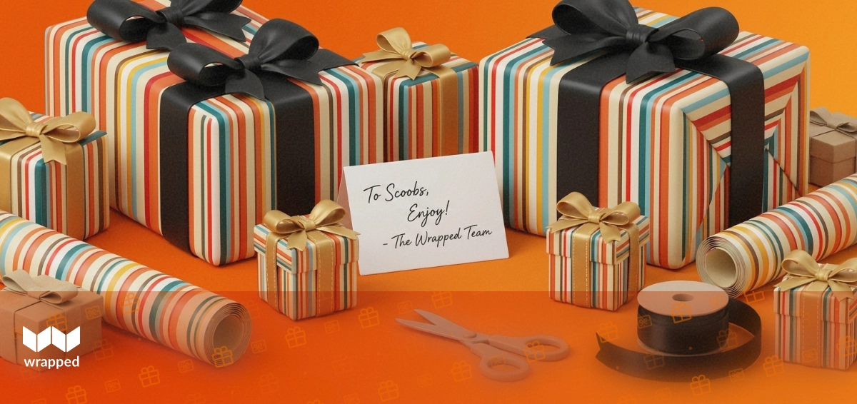 Wrapping paper roll, satin ribbon, handwritten message card and a small kraft gift box arranged on a warm amber table