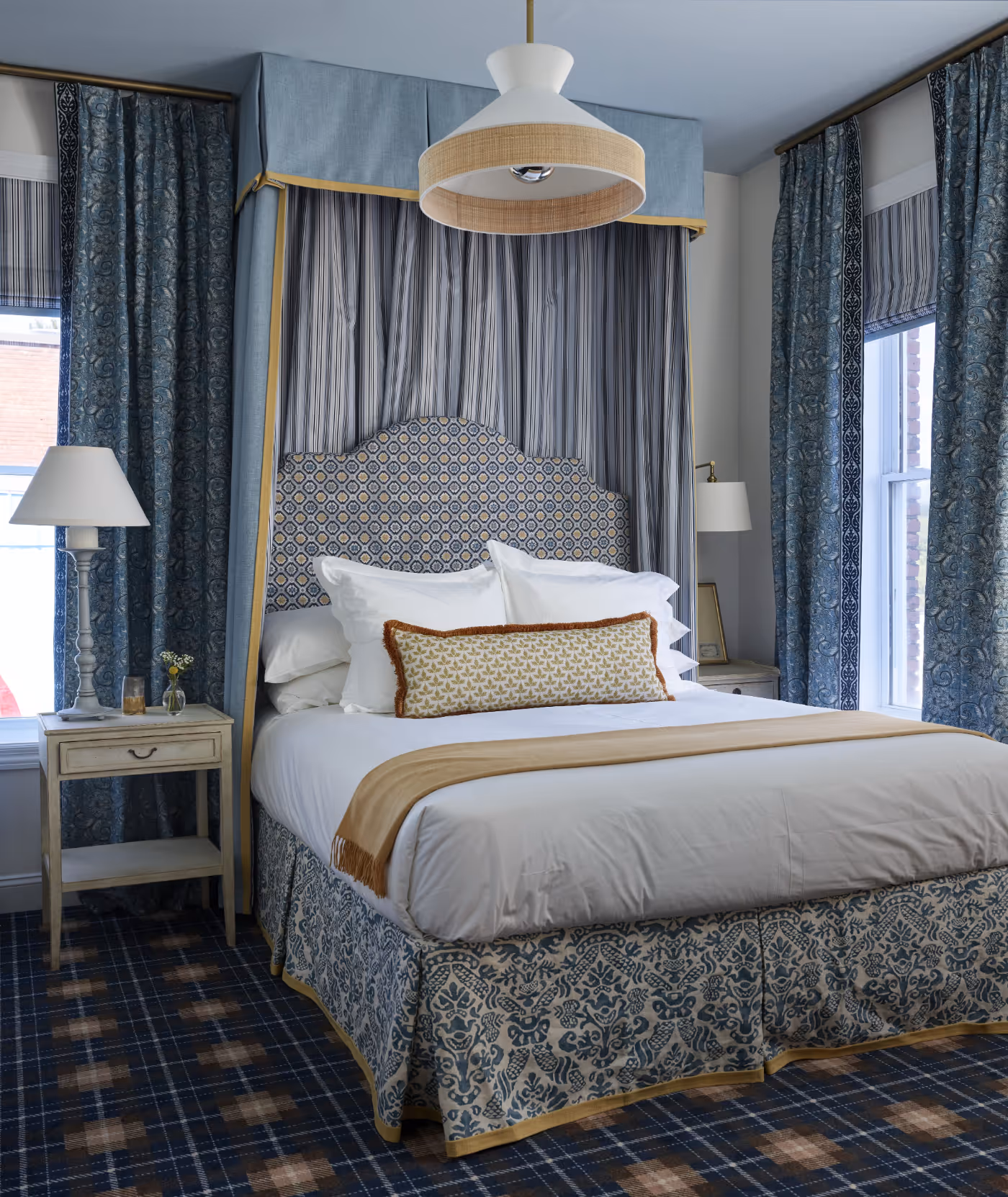 Elegant bedroom with a bed featuring a patterned headboard, white bedding, blue and gold decorative curtains, and a plaid carpet.