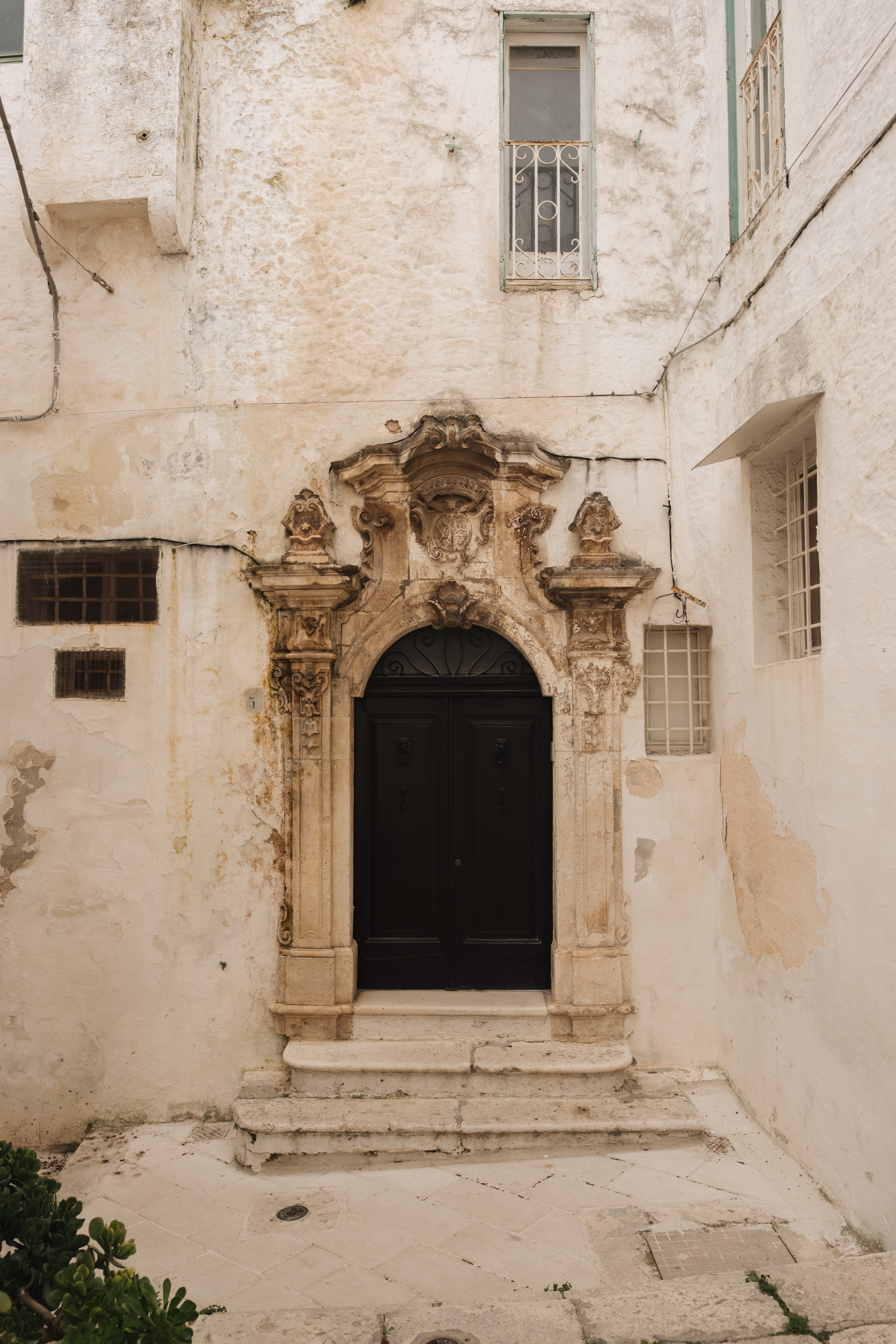 Baroque stone portal with a dark double door in a whitewashed courtyard