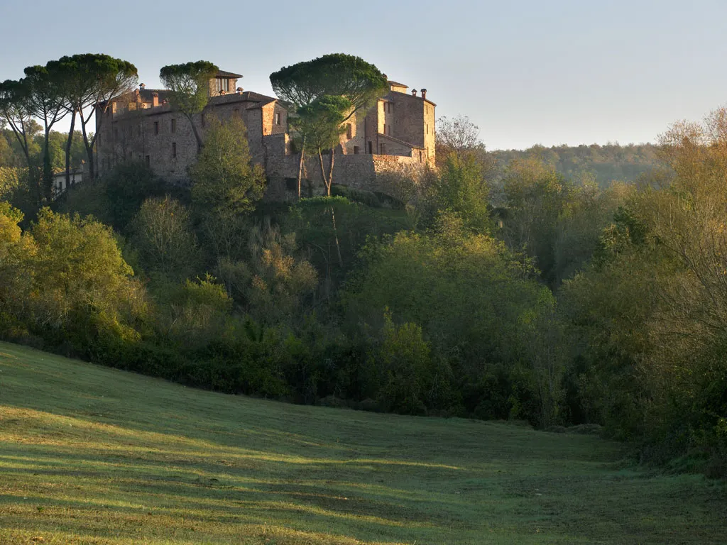 Castel Monastero on its wooded ridge near Castelnuovo Berardenga, in evening light