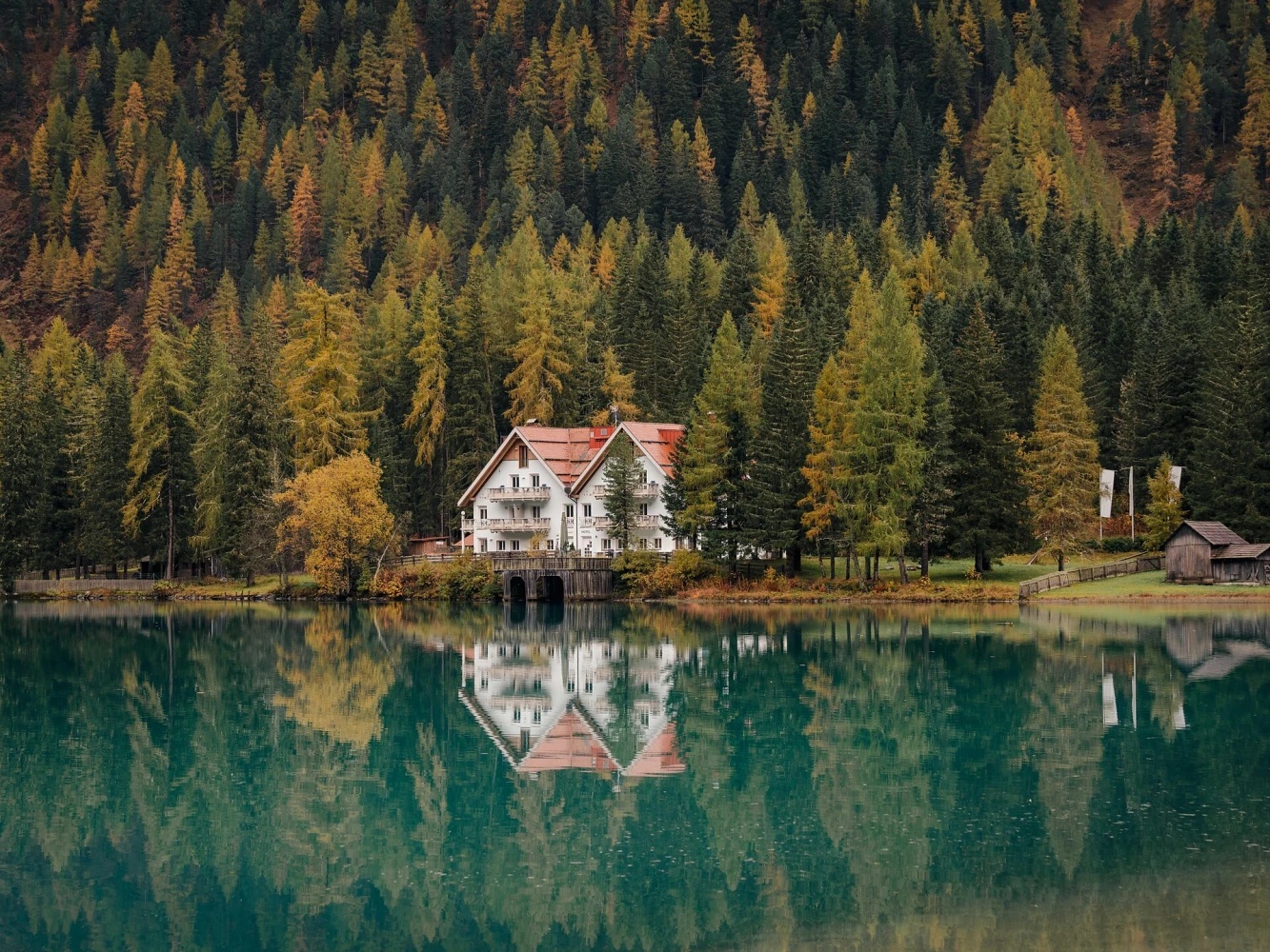 The Antholzer Wildsee Haus on the shore of the Antholzer See, reflected in the green water, autumn larches and spruce behind