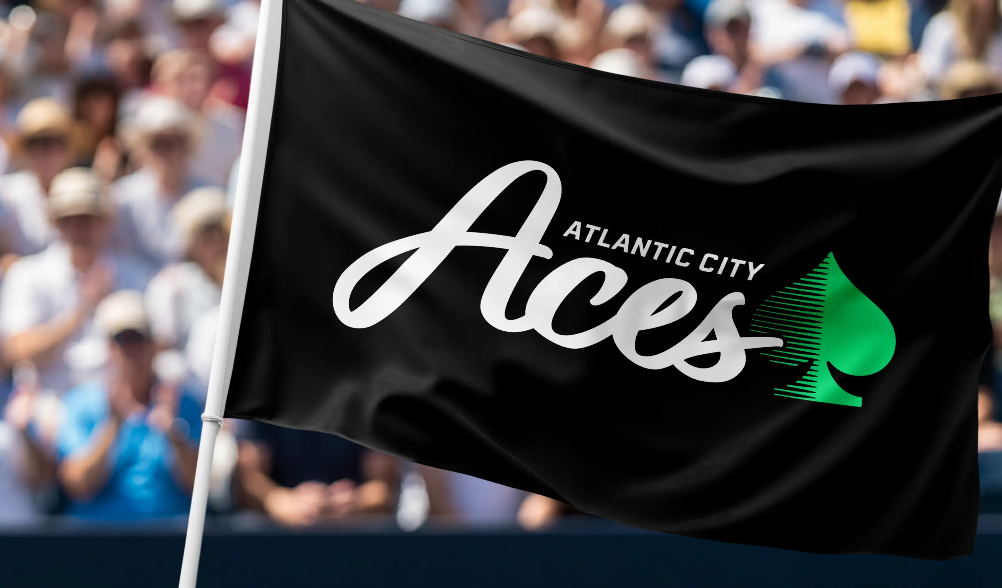 A black flag, with white text that says Atlantic City Aces and a green clover logo, waving in the wind in front of a crowd