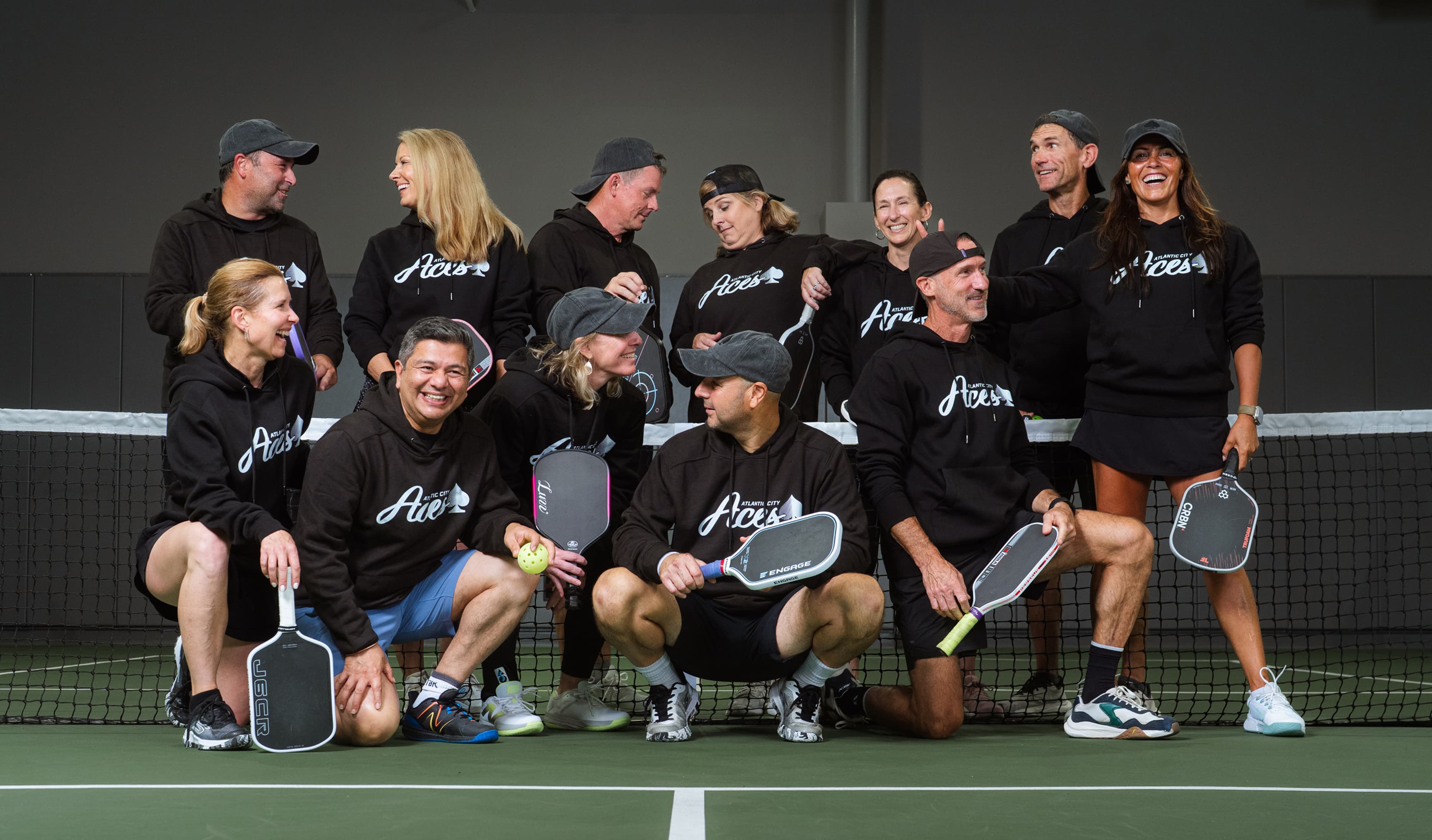 Group of 11 people in matching Atlantic City Aces hoodies posing on pickleball court with paddles.