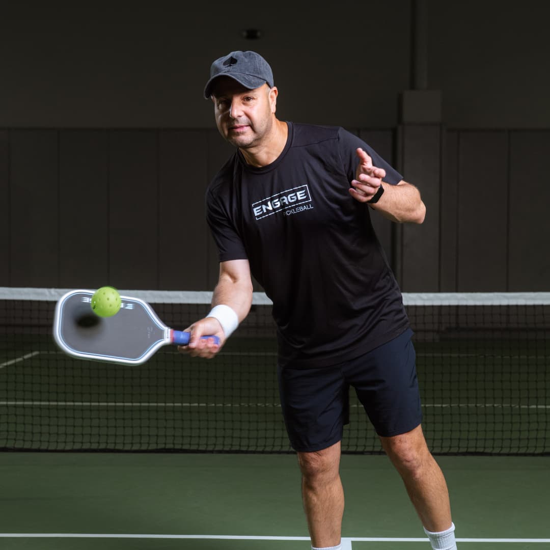 Profile picture of Youssef Bouzidi wearing a black Atlantic City Aces hat and a black Engage Pickleball t-shirt hitting a yellow pickleball with paddle.