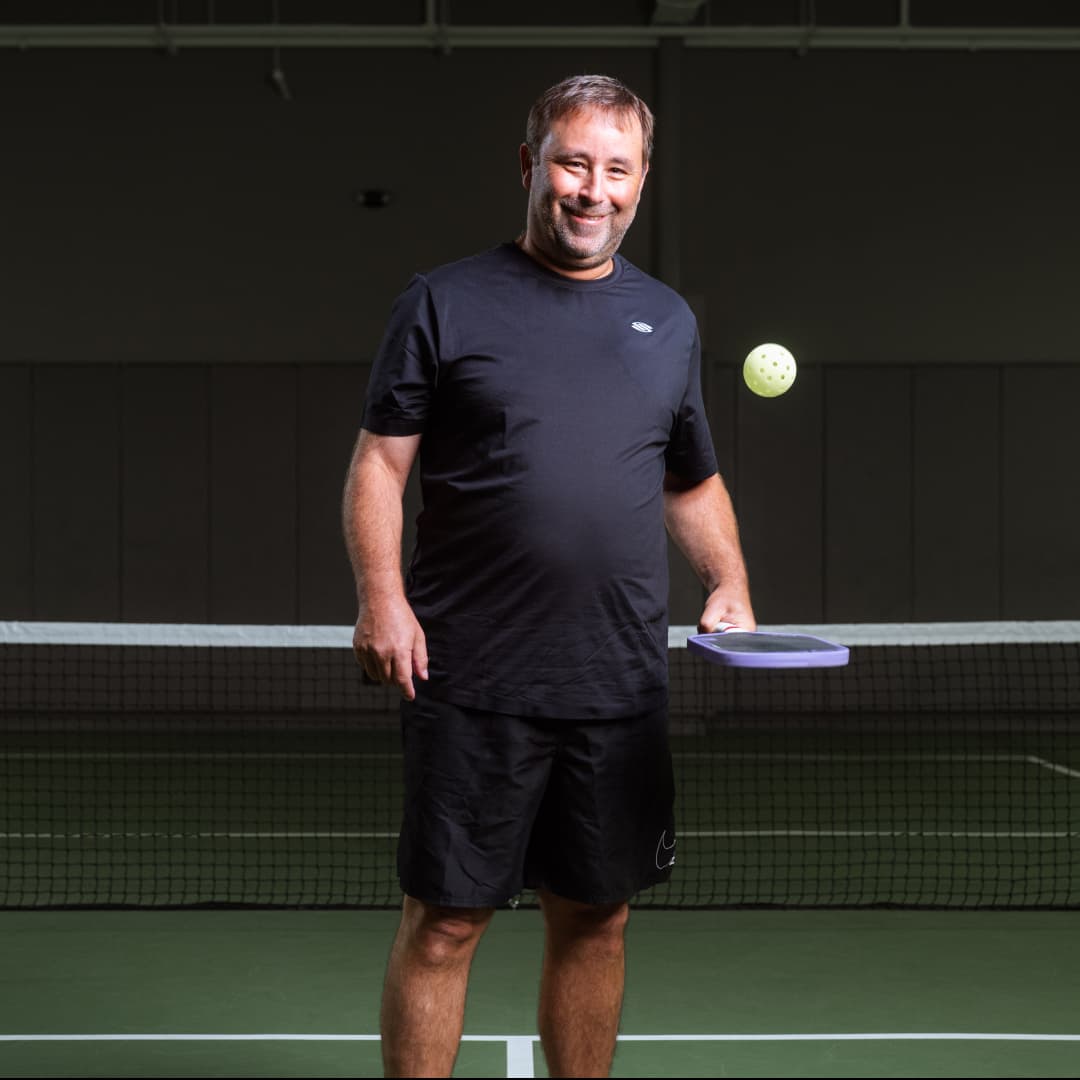 Profile picture of Ben Wenger wearing a black t-shirt with stylized 's' bouncing a pickleball with paddle.