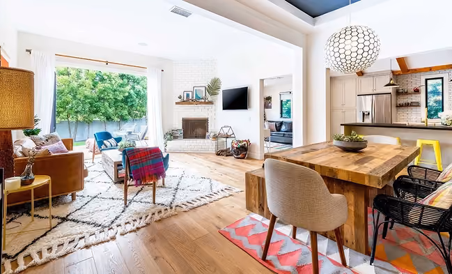 Bright, modern living and dining area with wooden furniture, colorful accents, and large windows.