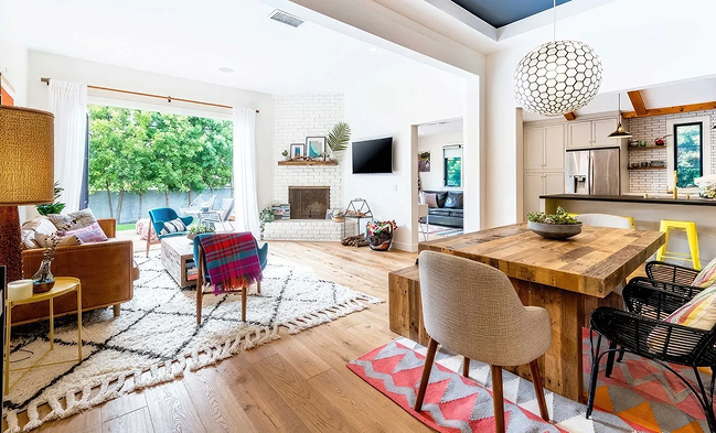Bright, modern living and dining area with wooden furniture, colorful accents, and large windows.