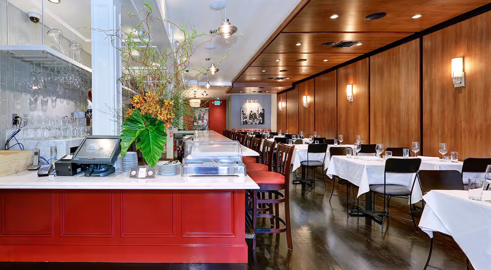 Modern restaurant interior with wooden panel walls, elegant table settings, and a red counter, showcasing thoughtful design and functional layout.