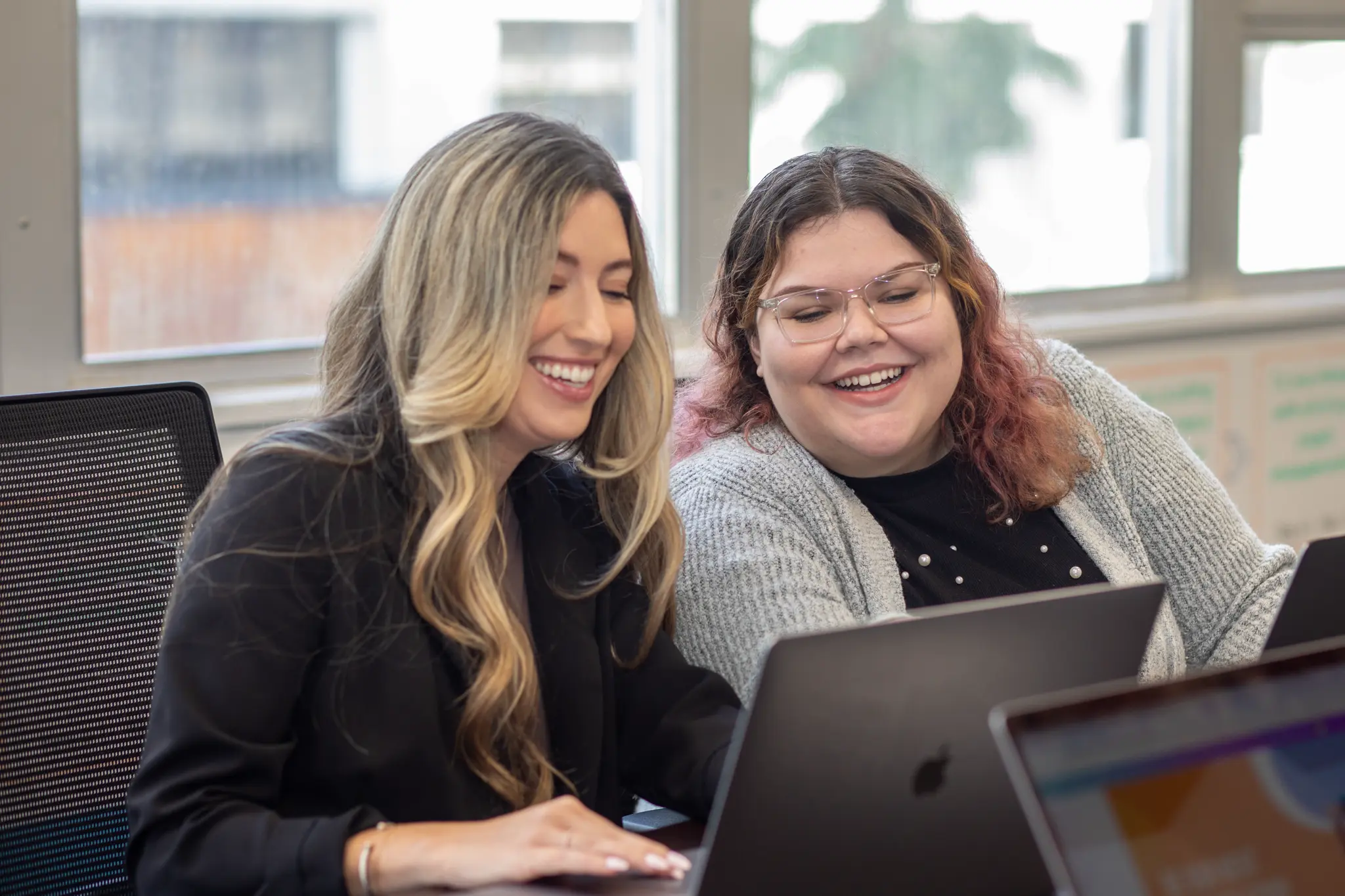 Two women smiling together while looking at a laptop
