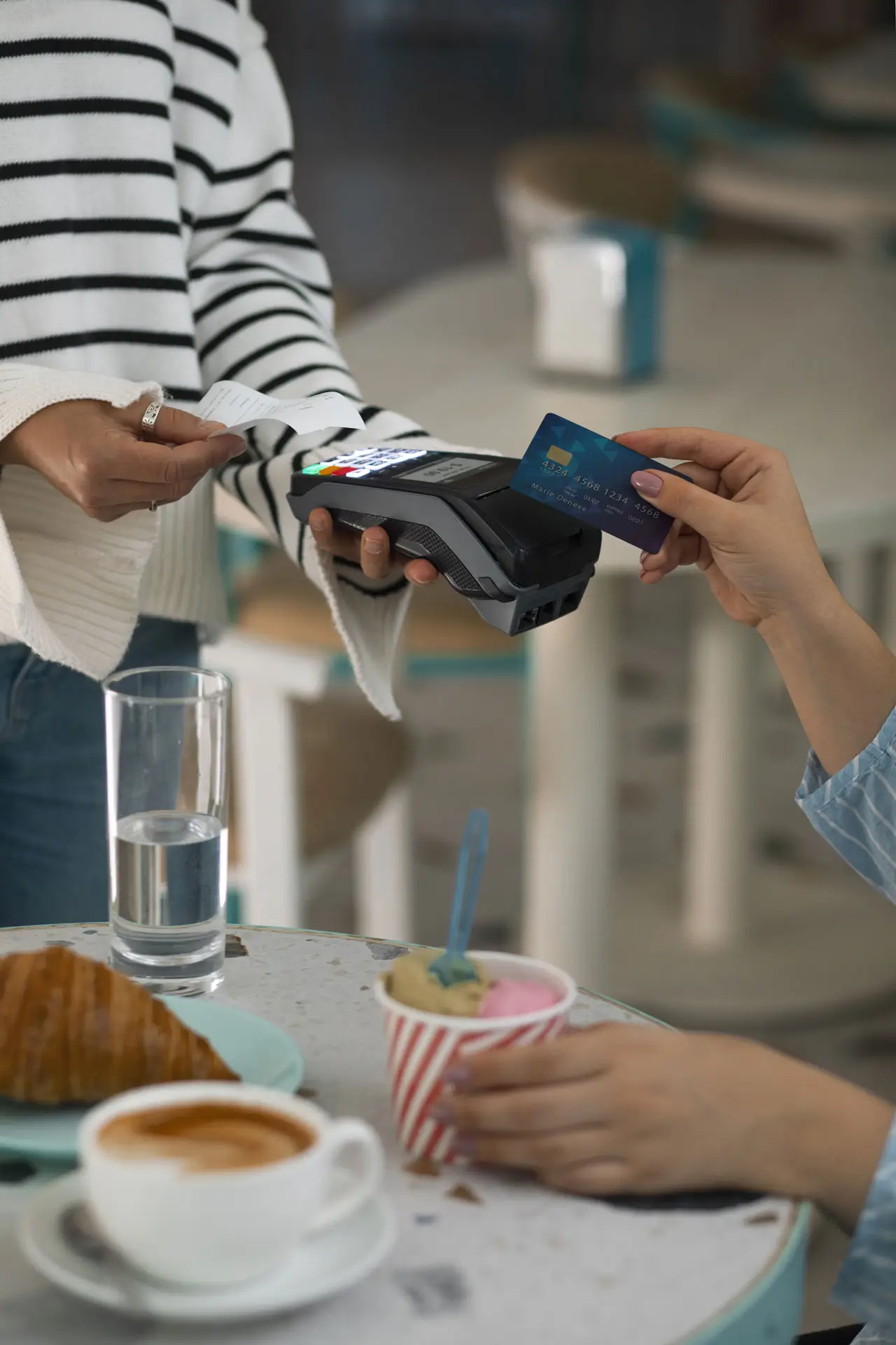 Cliente pagando con tarjeta sin contacto mientras persona sostiene terminal y recibo en cafetería.