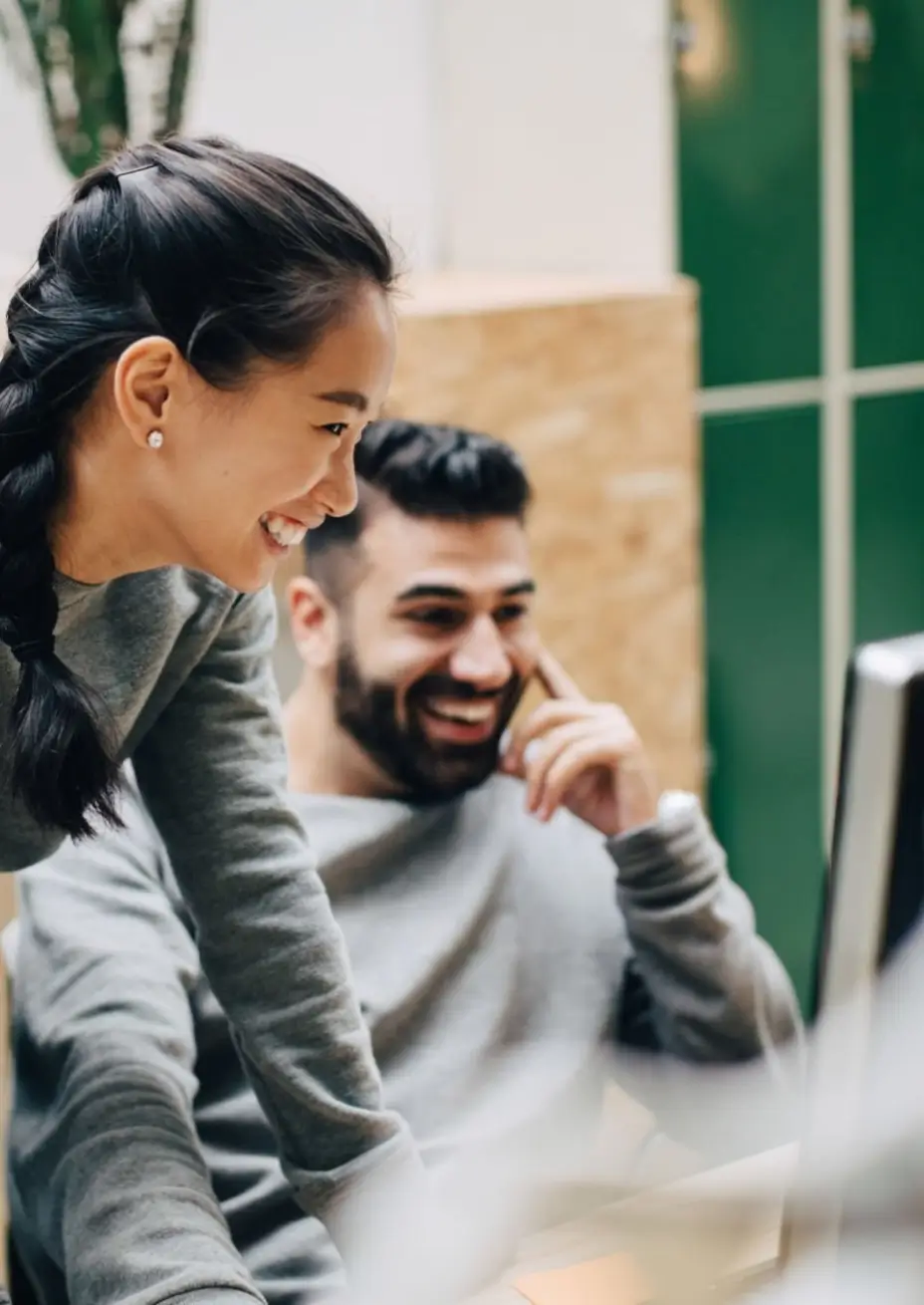 Dos colegas sonrientes y concentrados mirando una pantalla de computadora juntos.