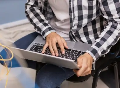 Persona usando laptop en su regazo, tecleando con una mano y sujetando el equipo con la otra.